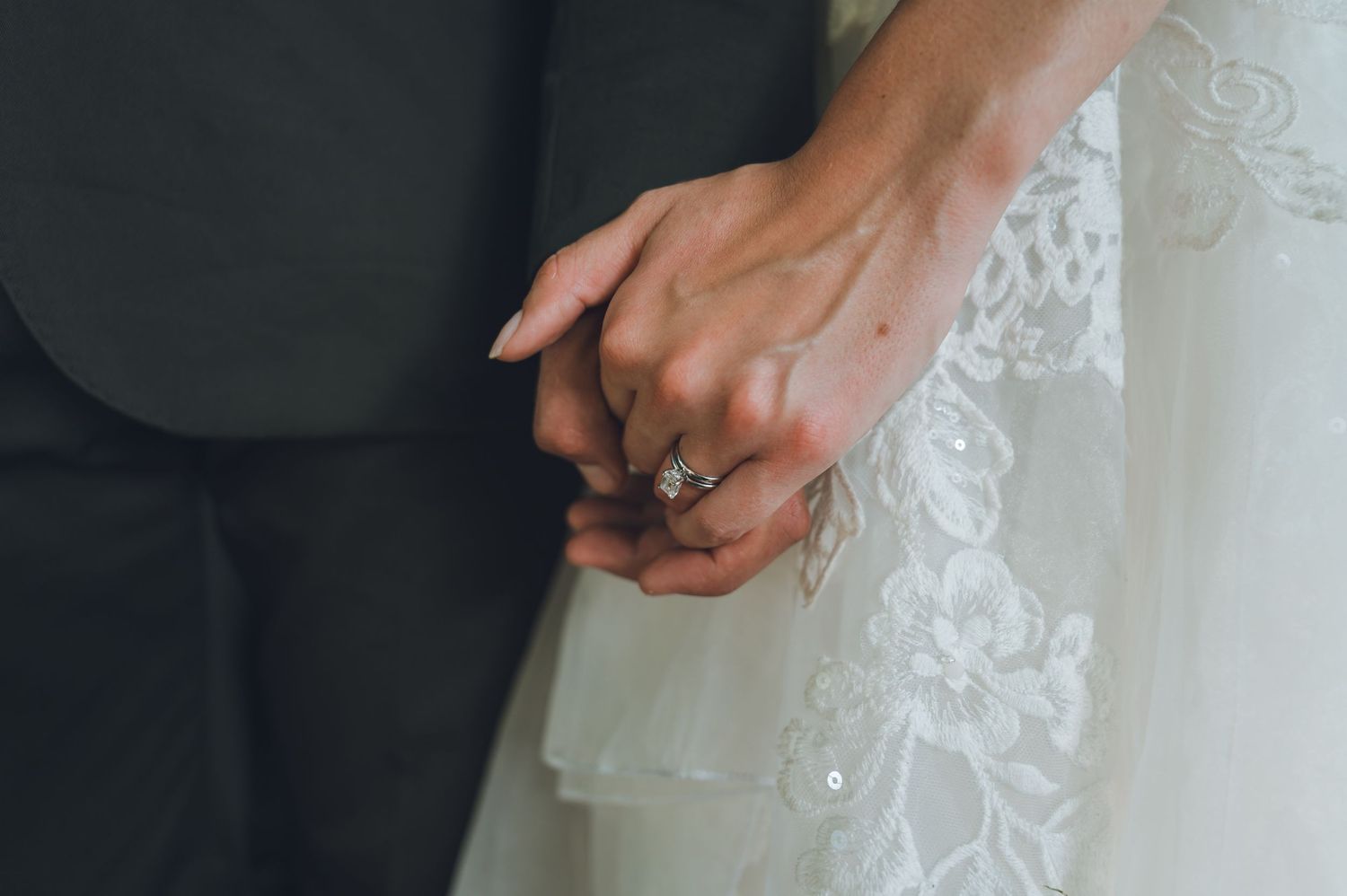 A close-up detail shot of an intricate white lace wedding dress with delicate floral embroidery patterns.