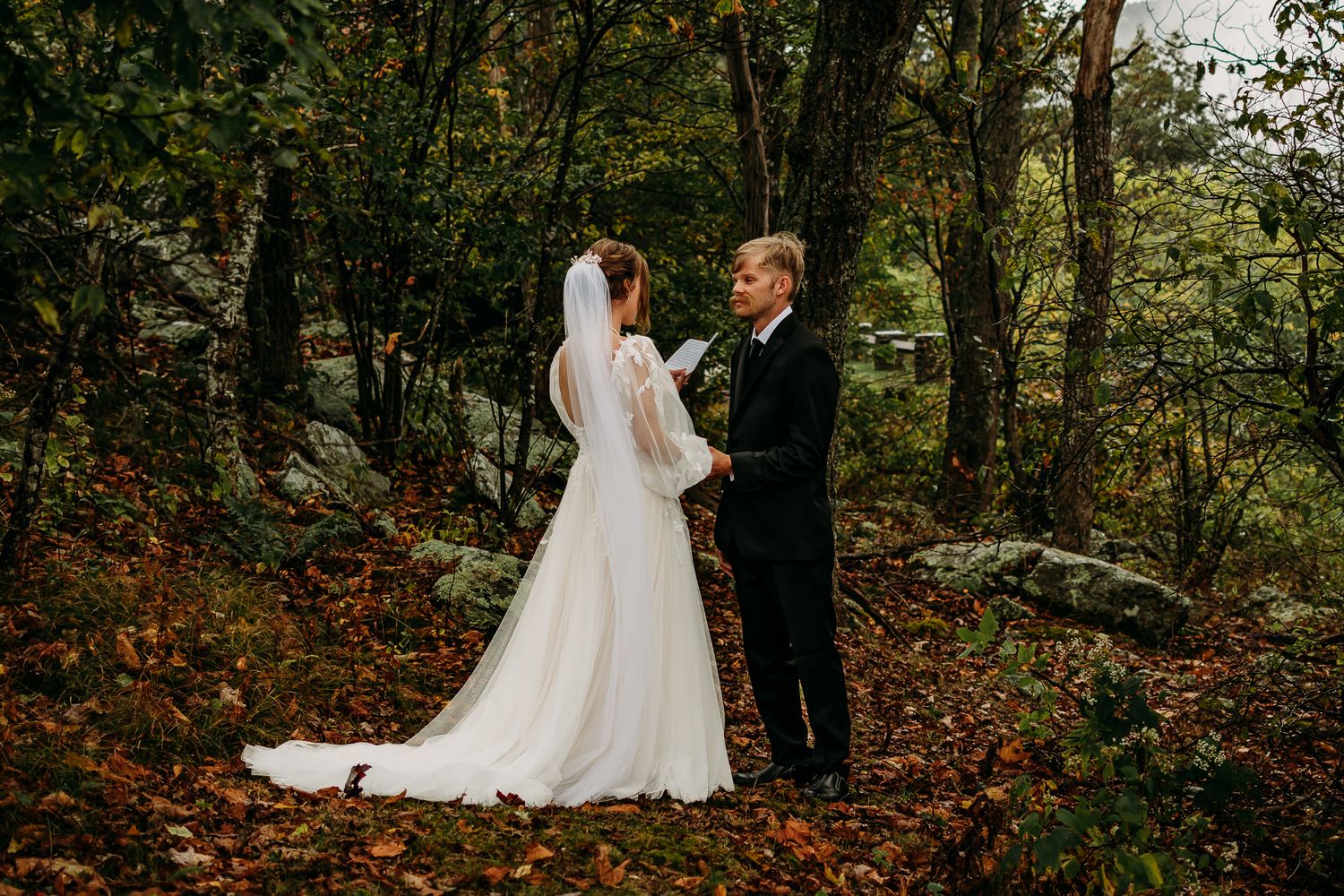 Wedding couple walking through autumn woods in traditional white dress and formal attire.