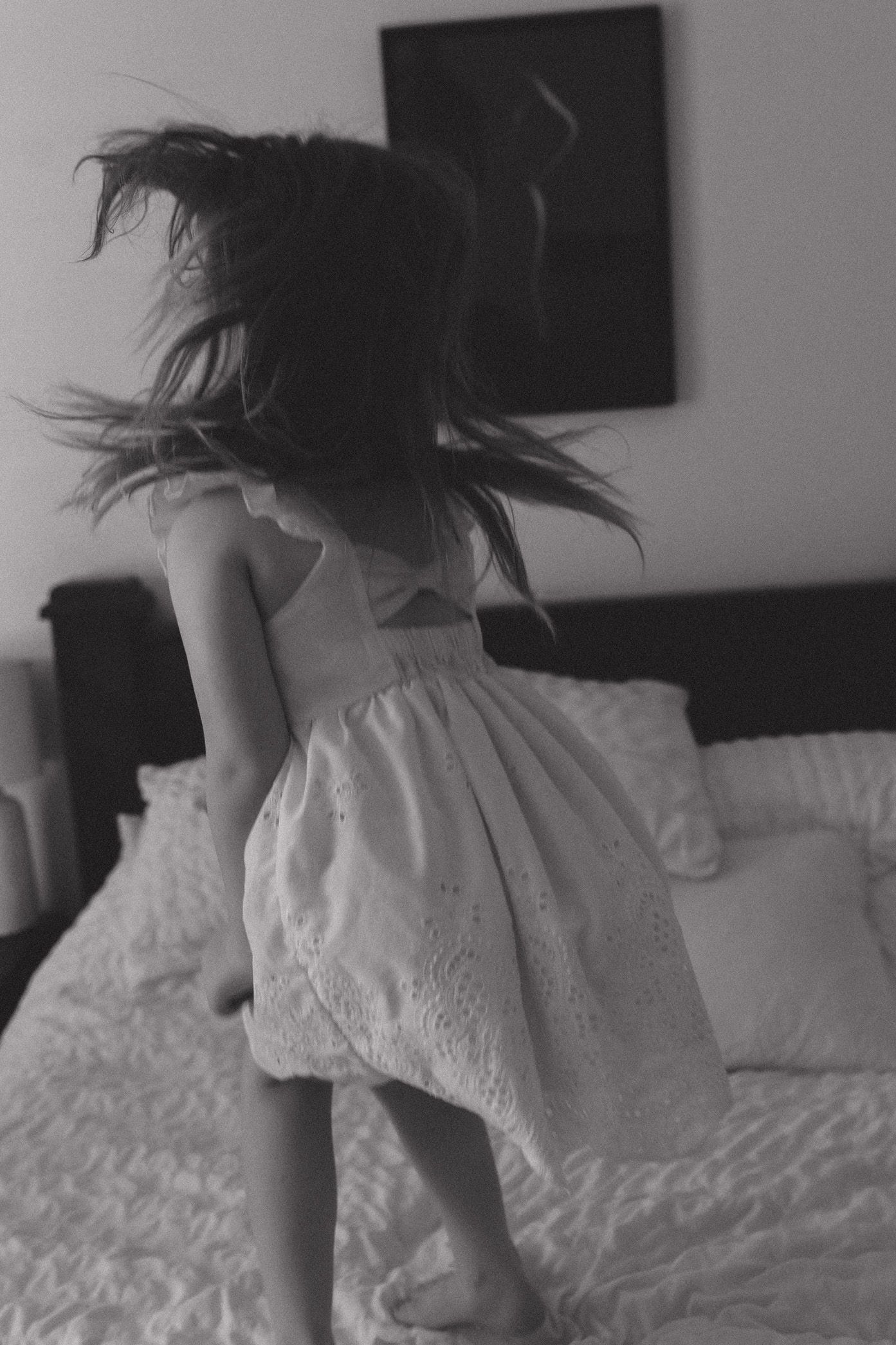 Black and white photo series showing someone jumping playfully on a white bed.