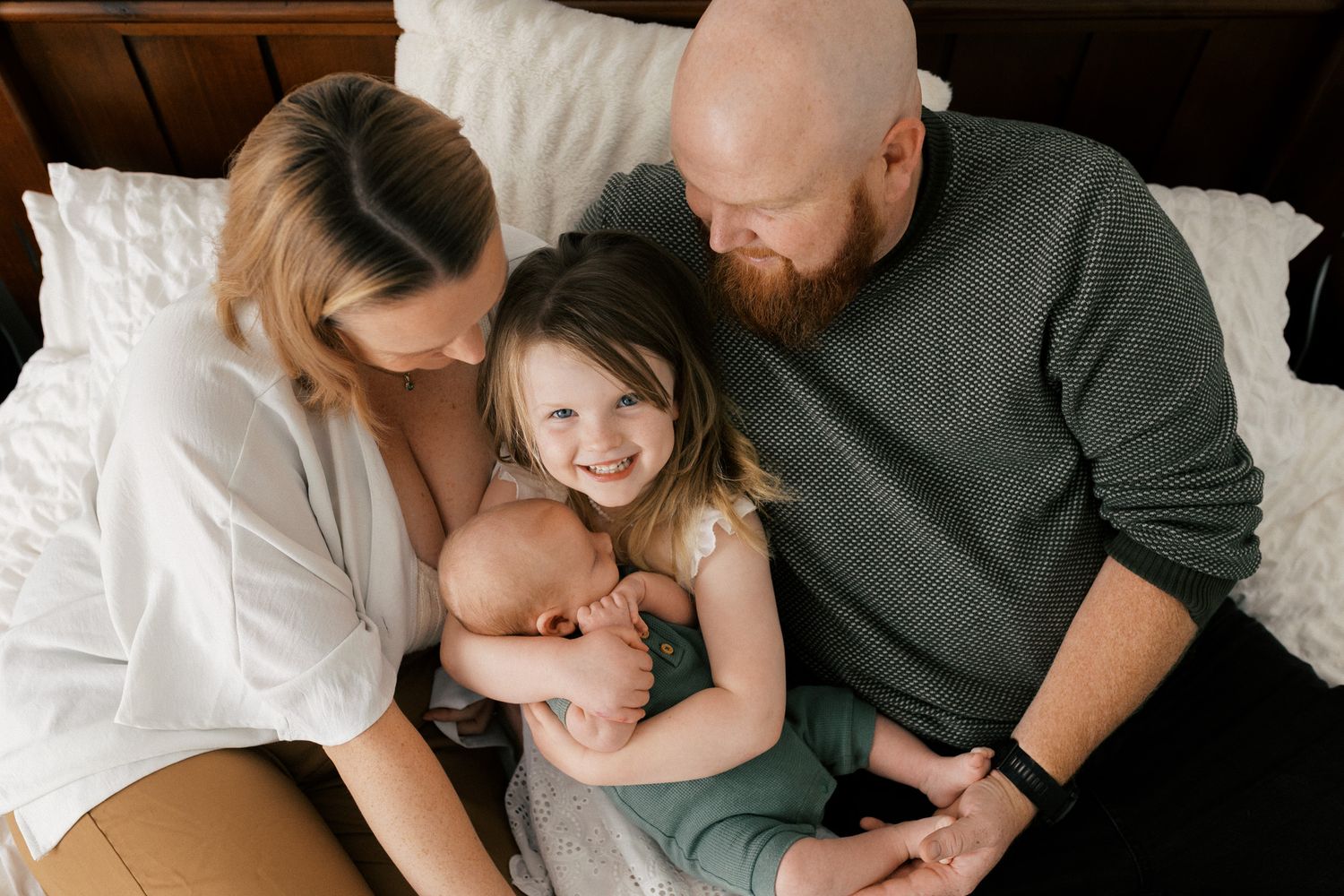 A family shares tender moments together while lounging on a white bed in matching casual outfits.