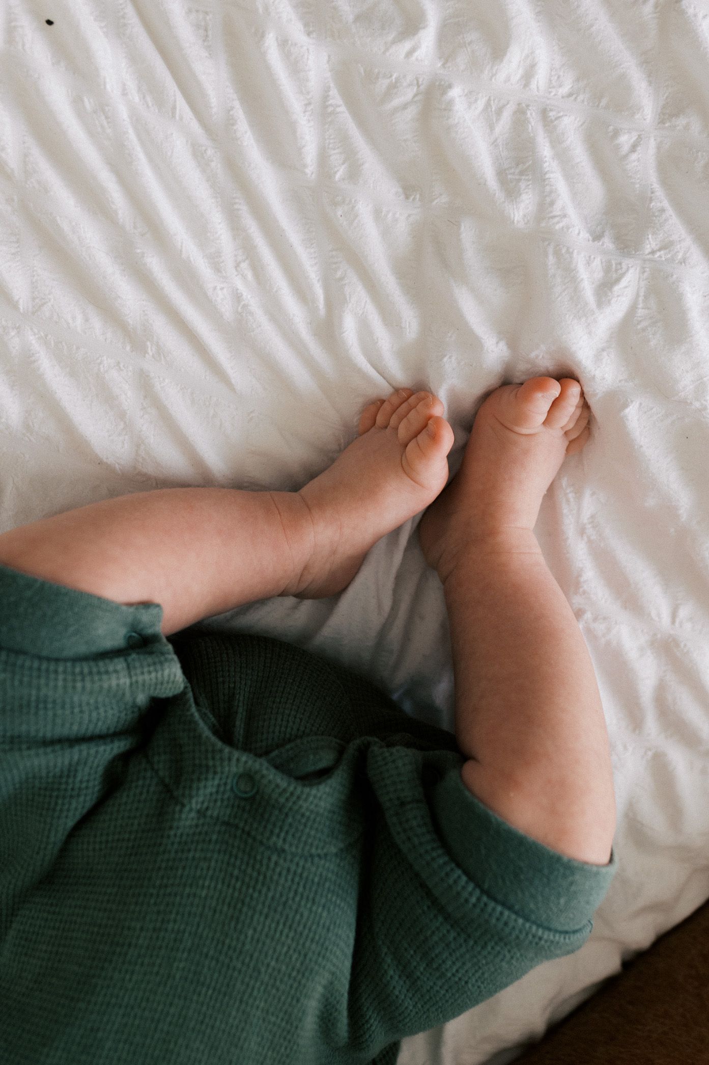 A series of baby feet photos arranged in a row showing tiny toes against white bedding.
