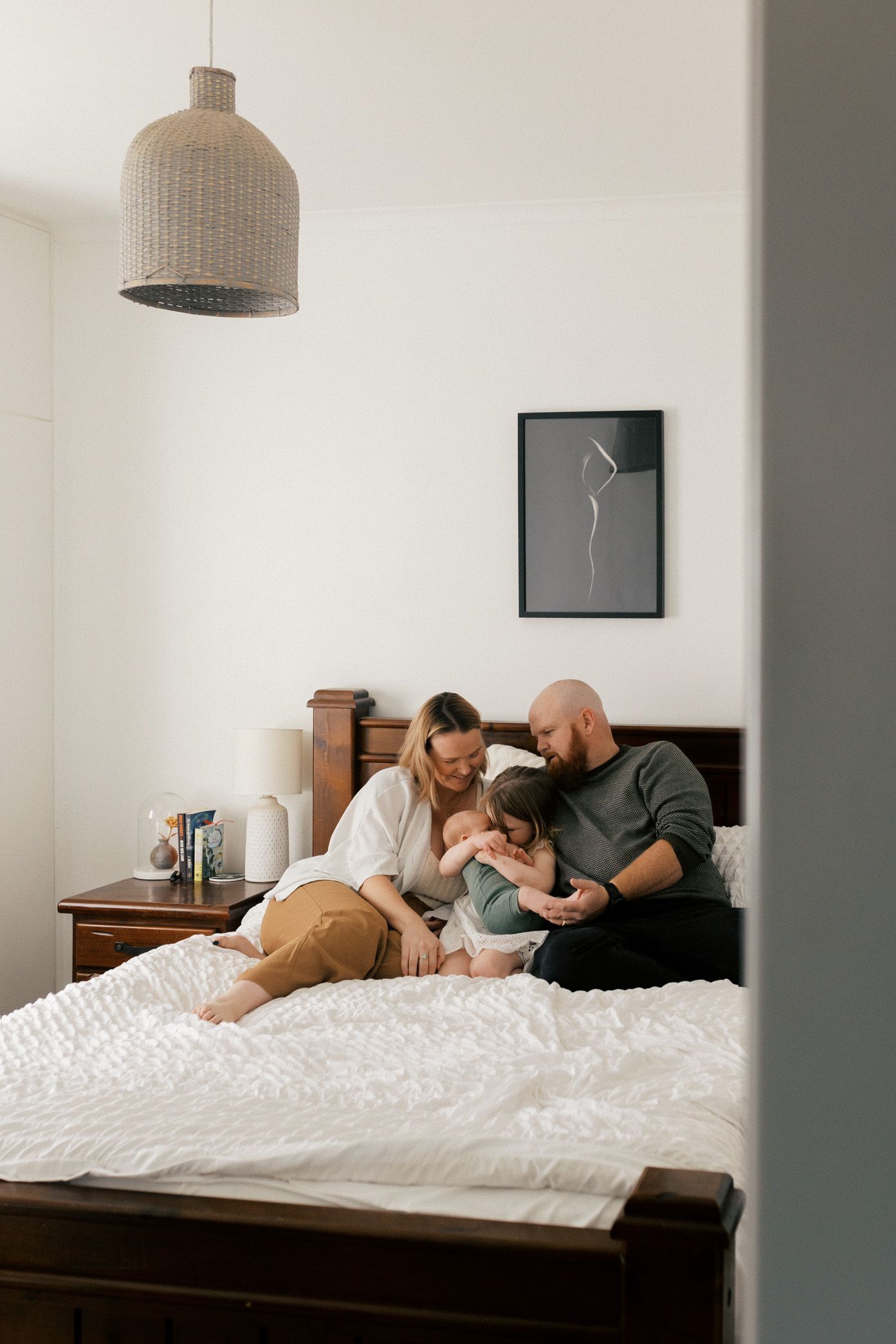 A couple relaxes together on a white bed in a minimalist bedroom with pendant lighting.