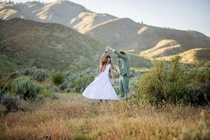 Couple dancing in a golden meadow with lush green hills in the background during sunset.