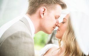 Bride and groom sharing a romantic kiss on their wedding day, with soft natural lighting and bokeh background.