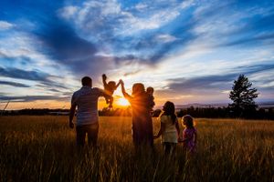 A family silhouetted against a dramatic sunset sky holds their child up together in a golden field.