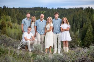 Family of seven posing outdoors in coordinated outfits with evergreen forest backdrop during golden hour.