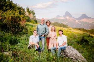 Group poses on grassy hillside with majestic mountain peaks rising in the background during golden hour.