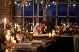A romantic candlelit reception table with couples sharing an intimate moment at sunset by large windows.