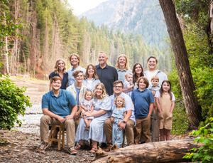 A group portrait taken outdoors in a mountain forest setting with tall evergreen trees and rocky peaks in the background.