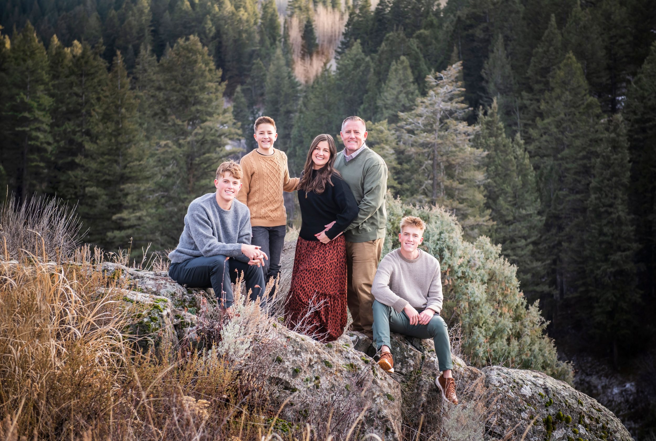 A scenic outdoor group photo on a rocky mountain overlook surrounded by evergreen forest in autumn.