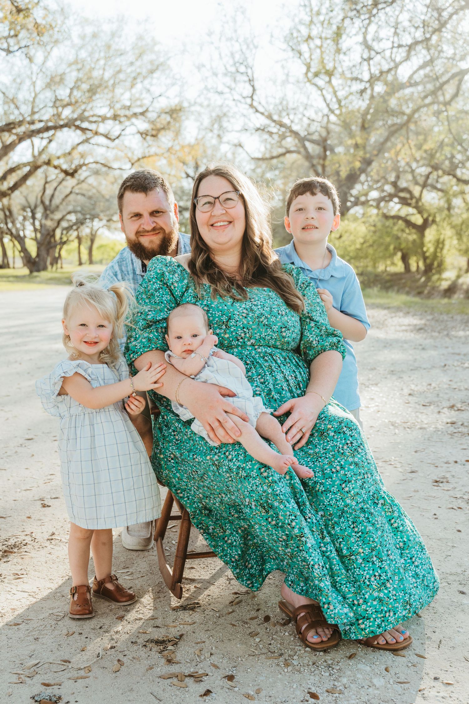Happy family of five posing outdoors on a sunny day, with parents and three young children in coordinating outfits.