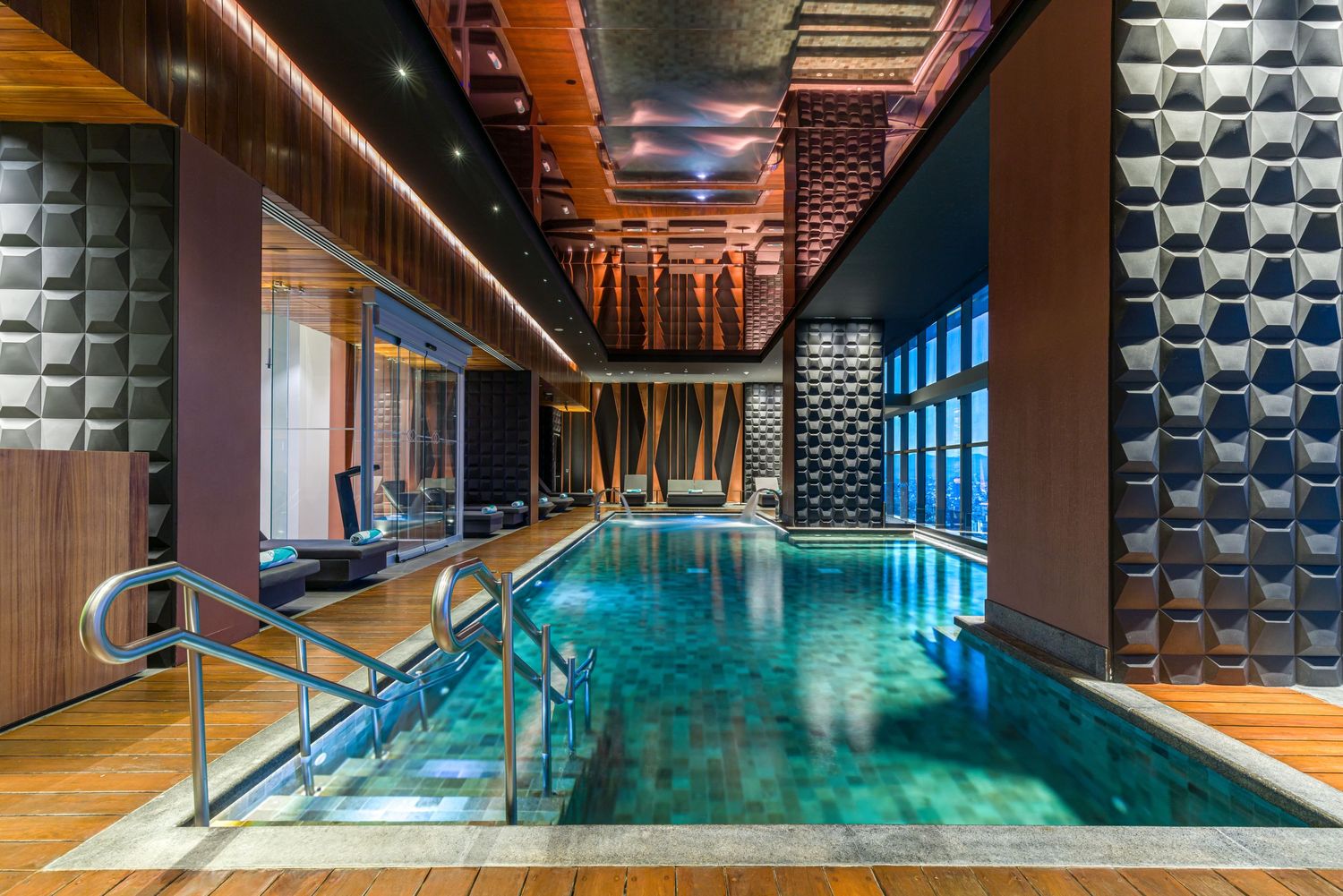 Luxurious indoor swimming pool with wooden walls, textured panels, and mood lighting in an upscale spa facility.