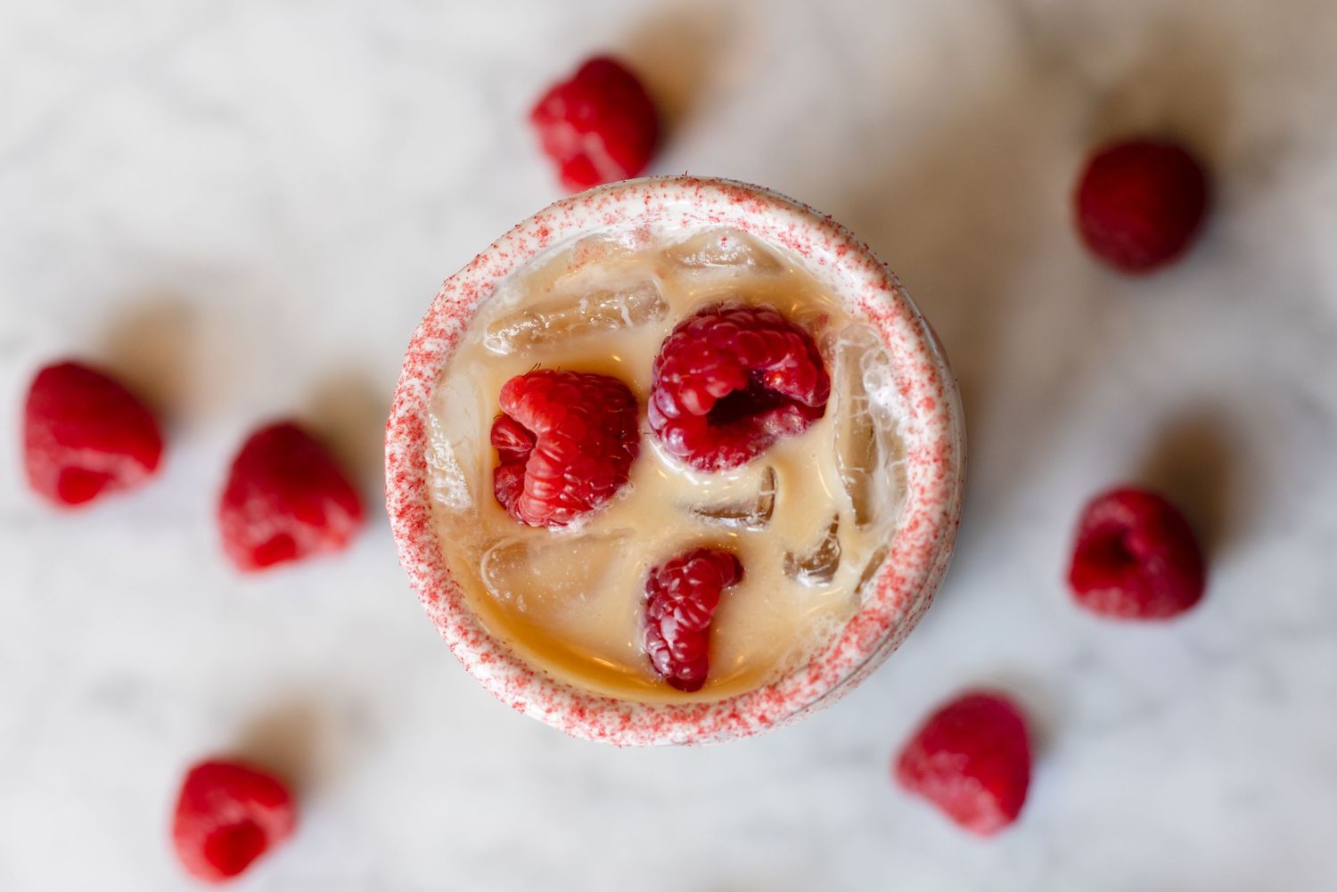 Refreshing summer cocktail garnished with fresh raspberries and ice cubes viewed from above on white background.