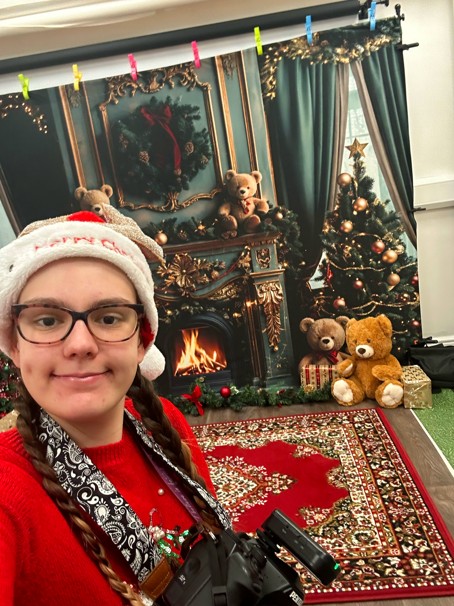 A cozy Christmas scene with a decorated tree, fireplace, teddy bears, colorful lights, and ornate decorations on a patterned rug.