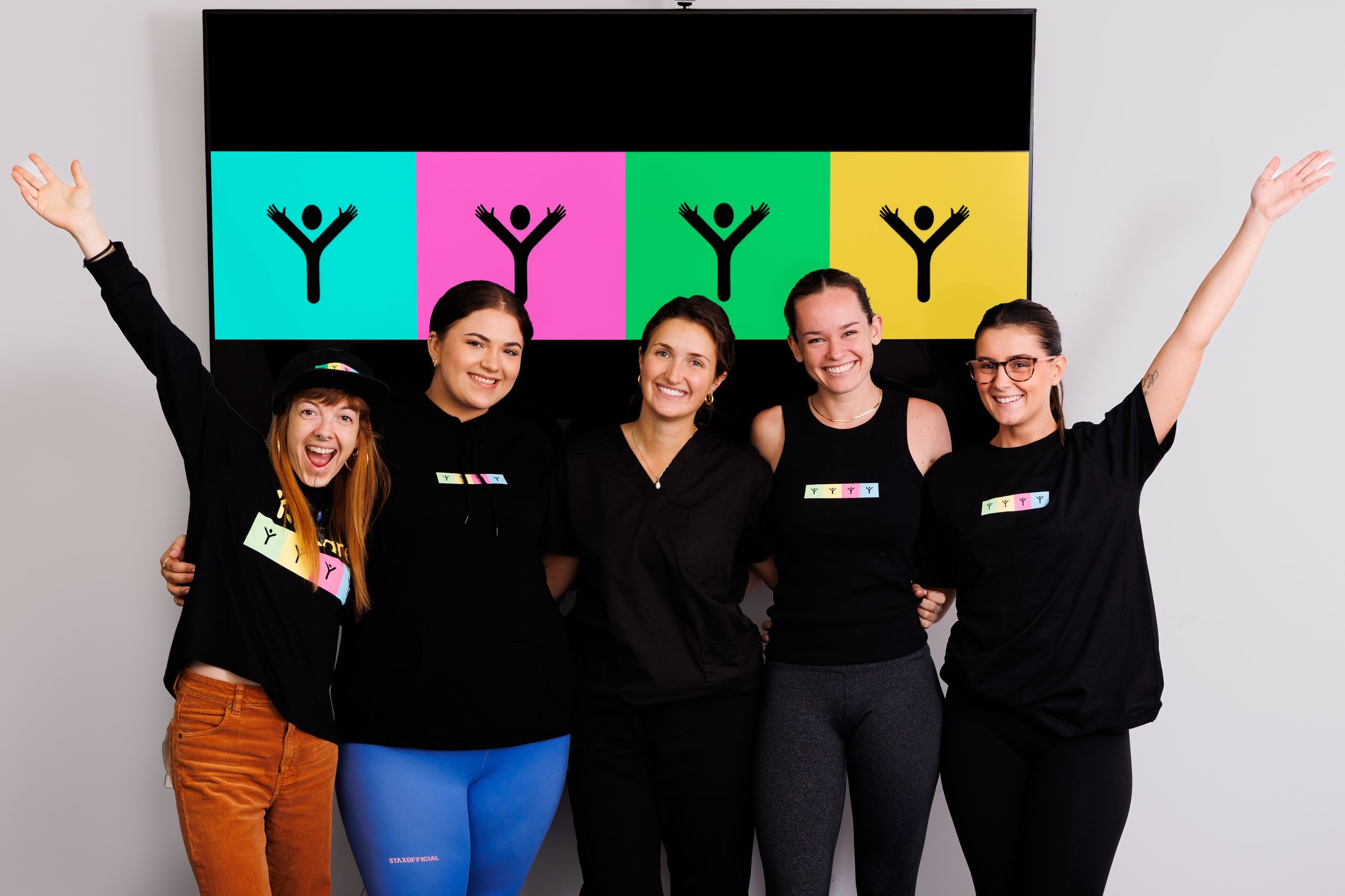 A group of people in black clothing pose together with raised arms and excited expressions.