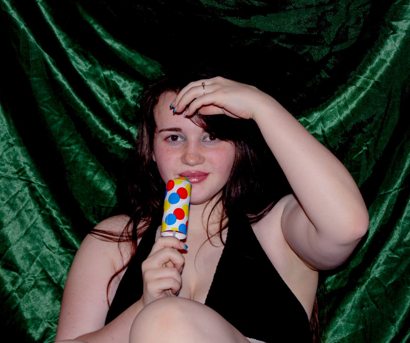 A person poses with a popsicle against a green velvet backdrop.