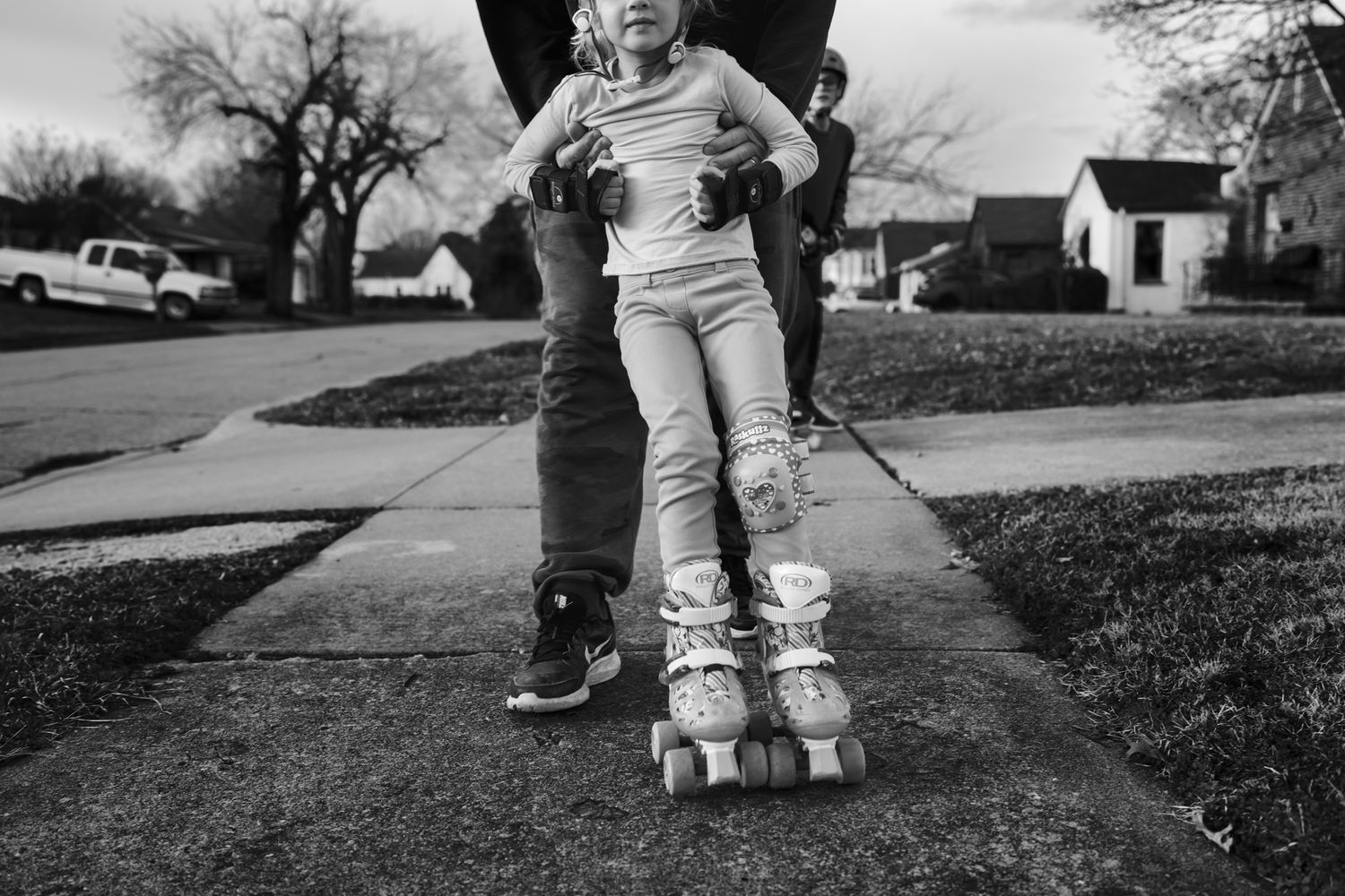 Little girl wears only one knee pad learning to skate with dad at family documentary photography session in Tulsa, Oklahoma