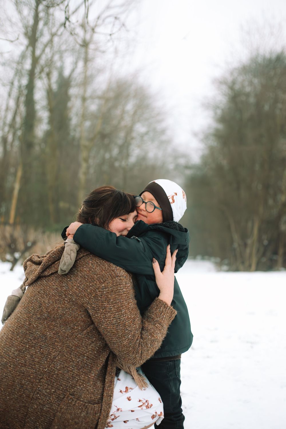 Moeder en zoon die een dikke knuffel geven in de sneeuw.
