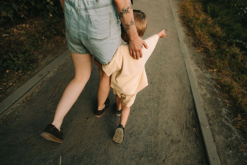 Adult holding toddler's hand while walking on a path outdoors, teaching baby first steps.