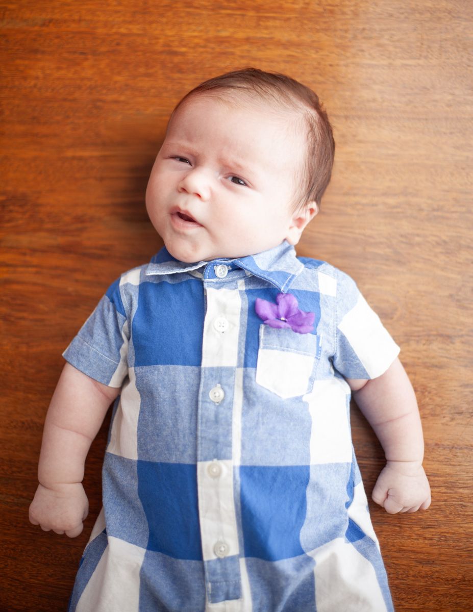 Baby lying on wooden surface wearing blue and white checkered outfit with purple bow tie.