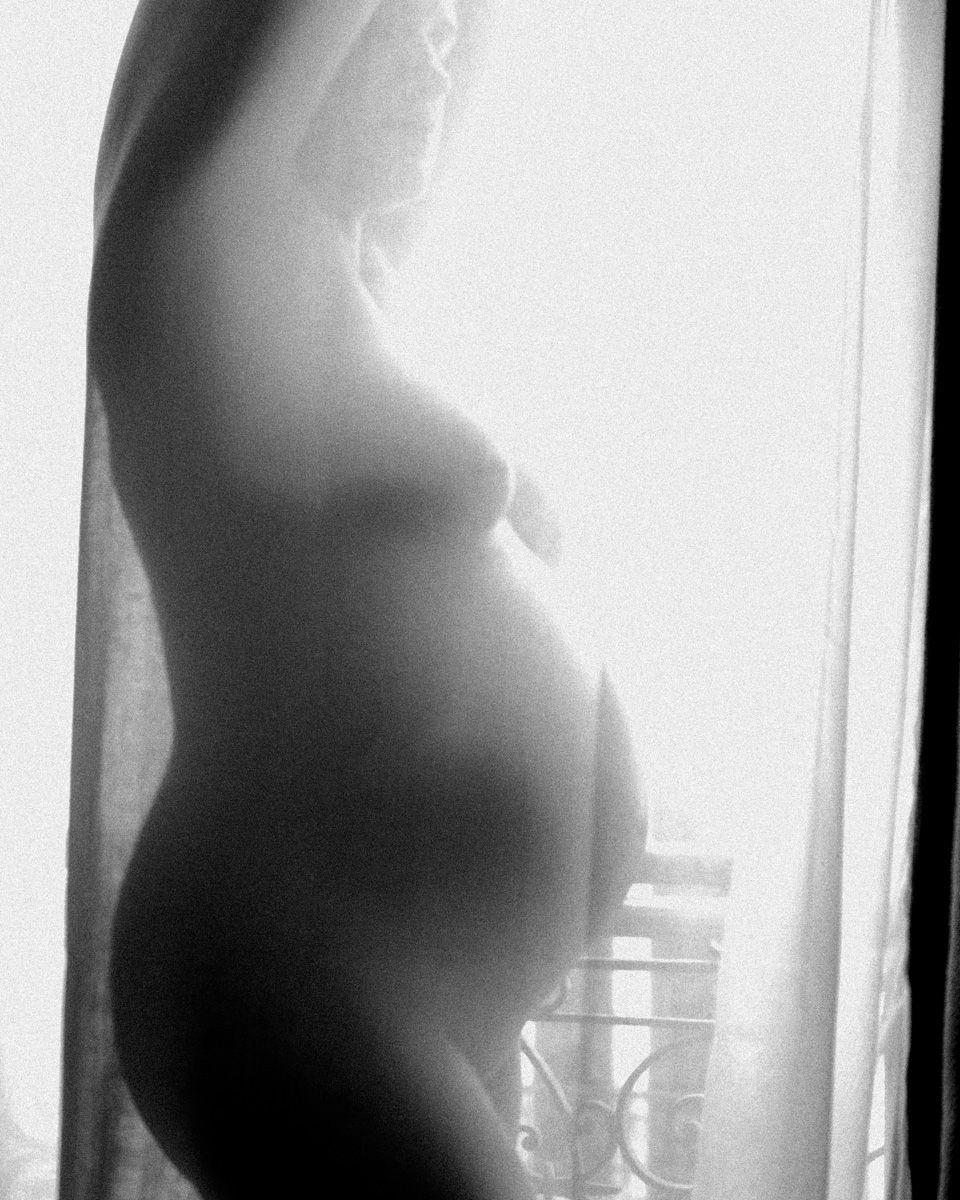 Black and white profile silhouette of pregnant belly with window light creating dramatic contrast.