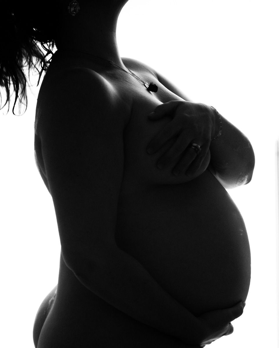 Artistic black and white silhouette photo highlighting a pregnant belly in profile against a light background.