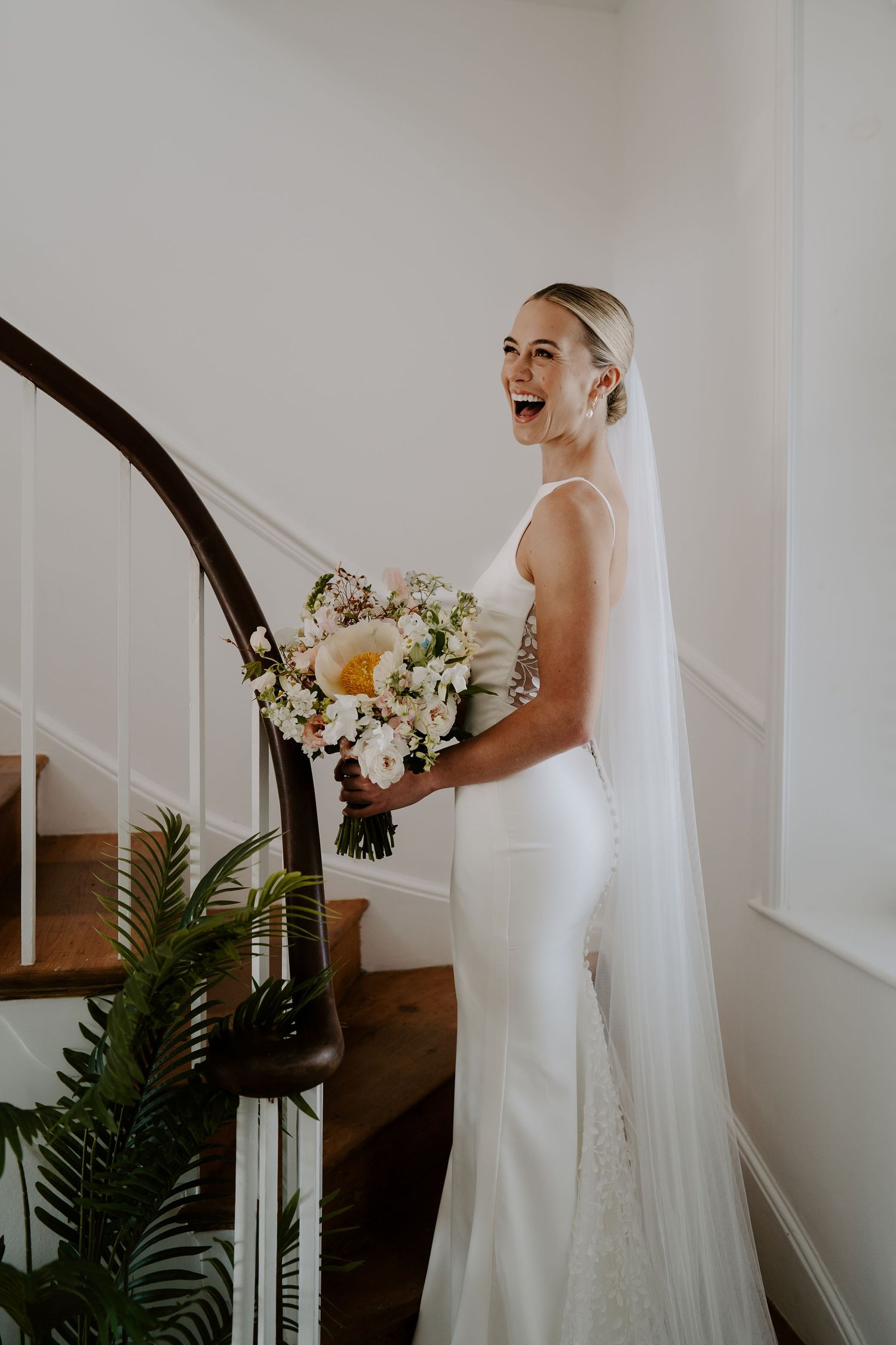 Tunnels Beach Wedding Venue in North Devon, Bride laughing with bouquet on stairs