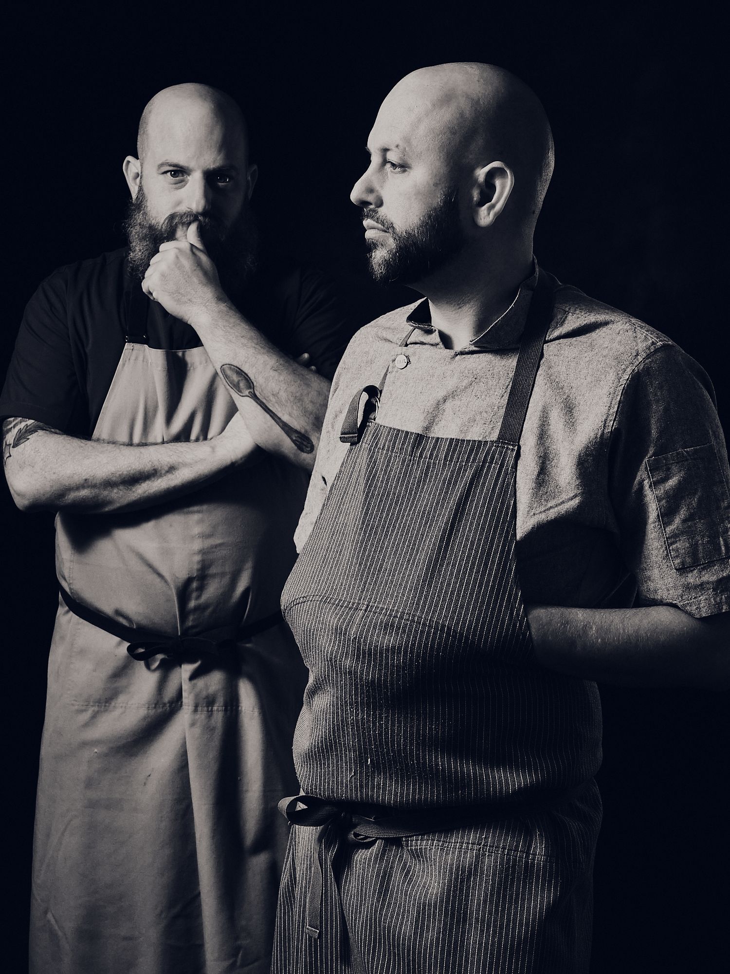Dramatic black and white portrait of two chefs in aprons.