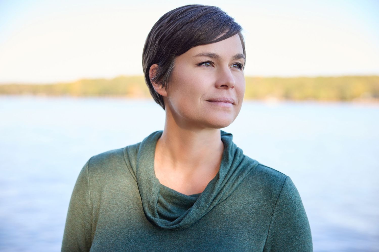 Portrait of a person in a green cowl neck sweater against a waterfront backdrop.