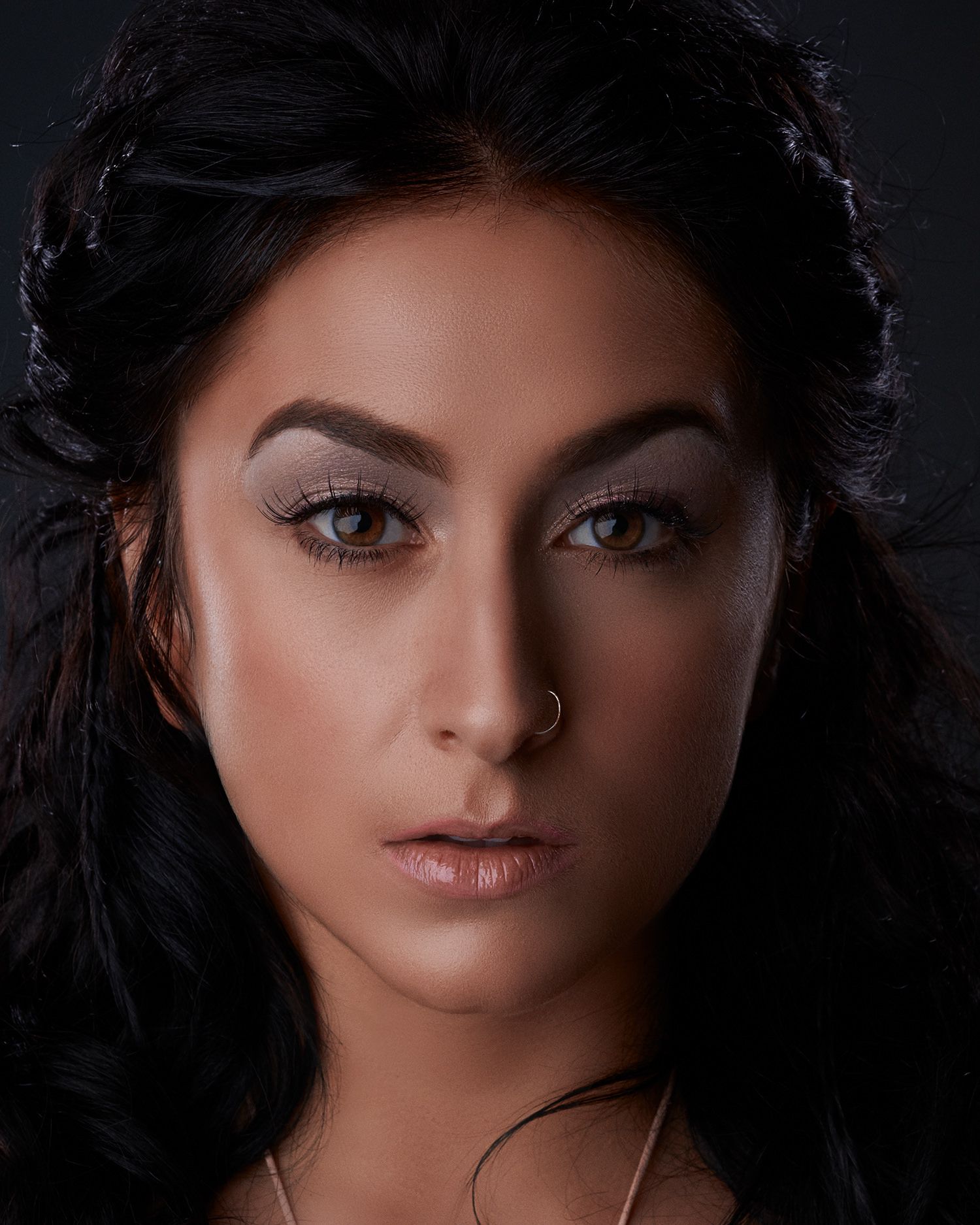 Beauty portrait with dramatic lighting showcasing flawless makeup and dark hair.