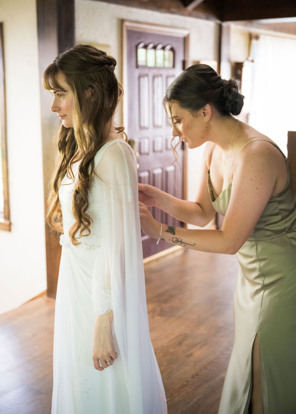 Wedding dress being adjusted and prepared in a sunlit room with wooden floors.