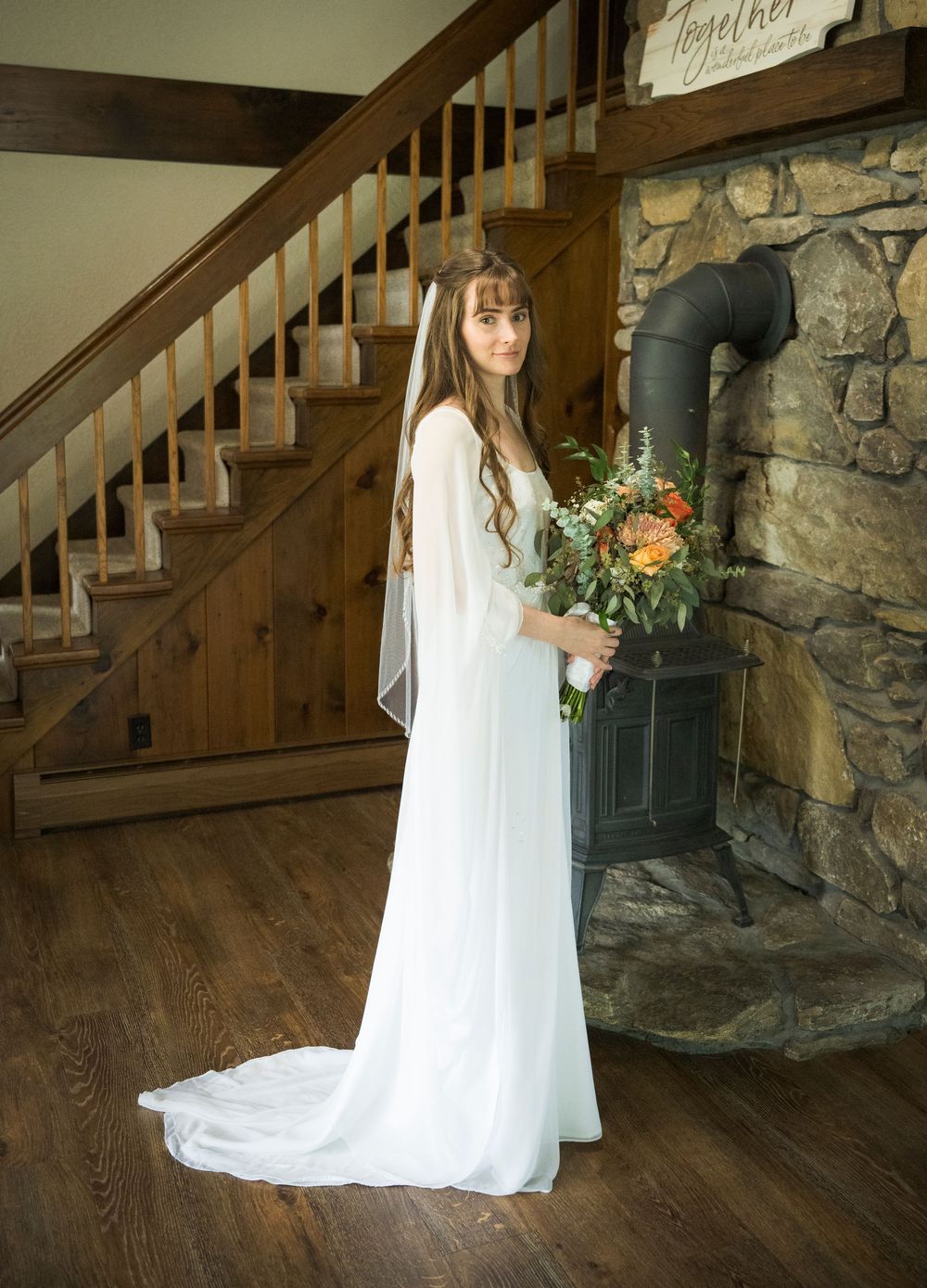 A flowing white wedding dress captured in a rustic indoor setting with stone walls and wooden stairs.