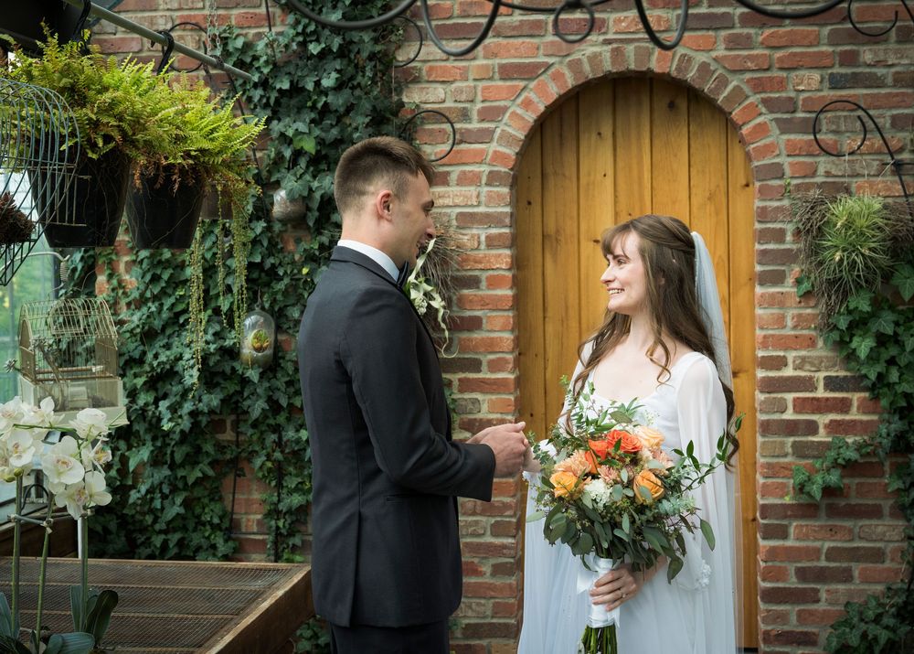 Wedding couple posing by a brick archway decorated with climbing vines and greenery.