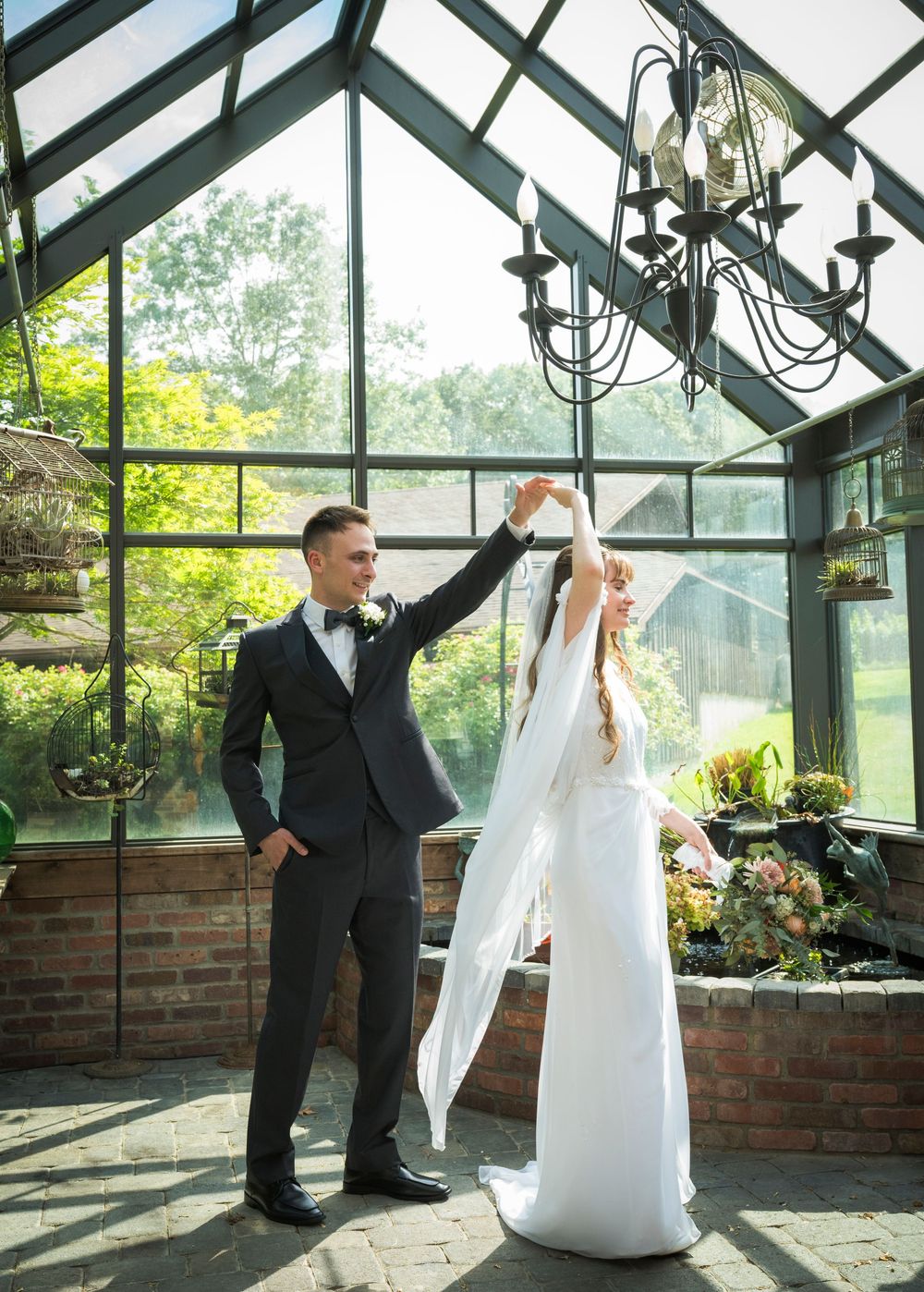 A couple shares a romantic dance moment in a sunlit greenhouse surrounded by lush greenery at their wedding celebration.