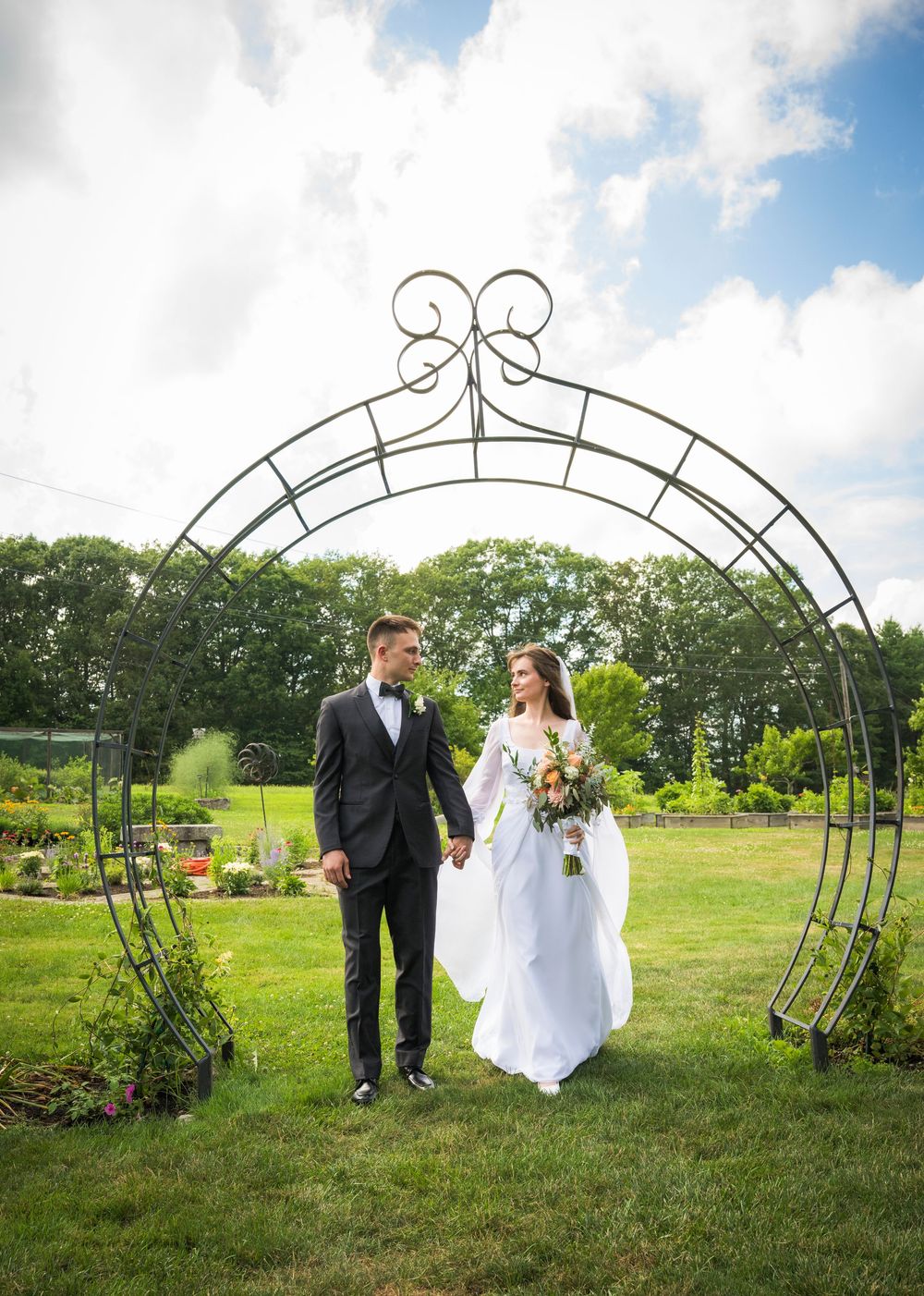 Wedding photography session under a decorative metal garden arch in a lush green field.