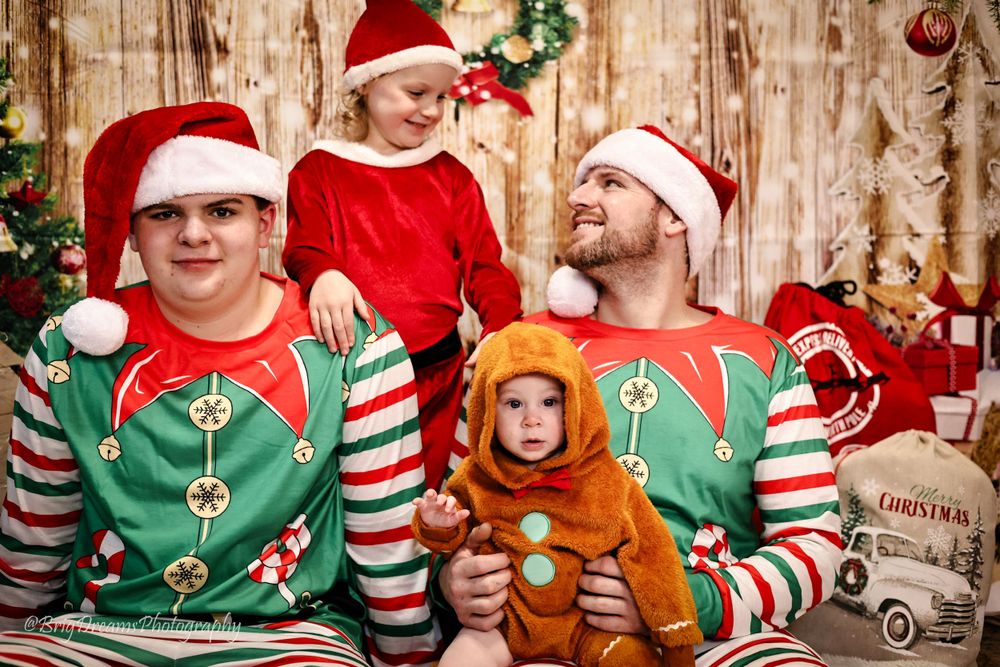 A family in matching Christmas elf sweaters and Santa hats pose together for a festive holiday photo against a rustic backdrop.