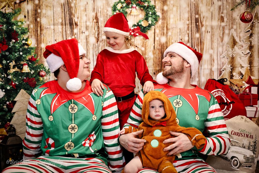 A family in matching Christmas elf pajamas poses together by a decorated tree with festive holiday decorations.