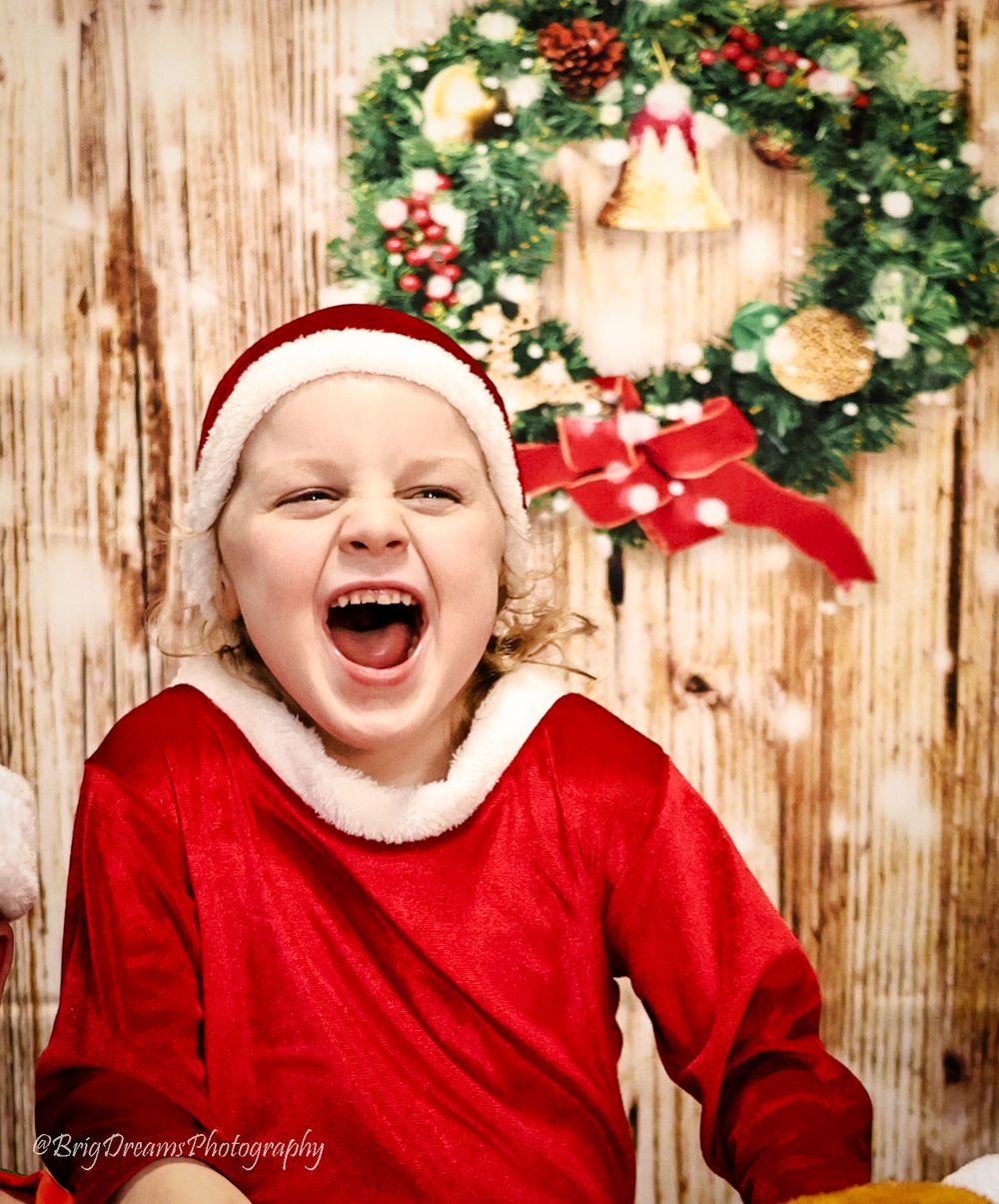 A festive Christmas scene with red holiday attire and joyful laughter against a wooden wall with decorative wreath.