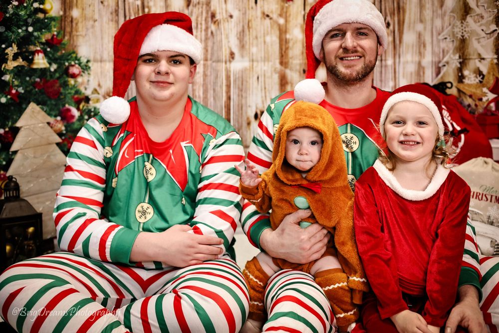 People wearing festive Christmas pajamas and Santa hats pose together with a Christmas tree in the background.