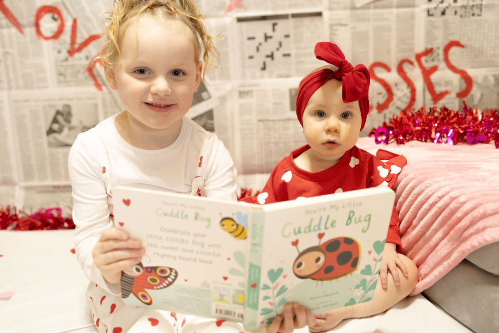 Two children in Valentine's themed outfits read a ladybug storybook together.