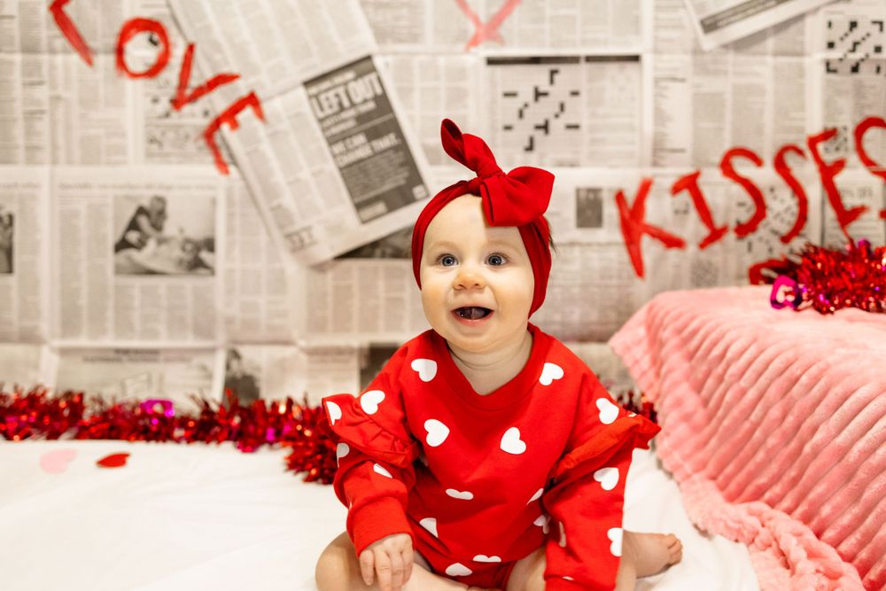Festive Valentine's photo with red heart-print outfit against newspaper wall with 'LOVE' text.