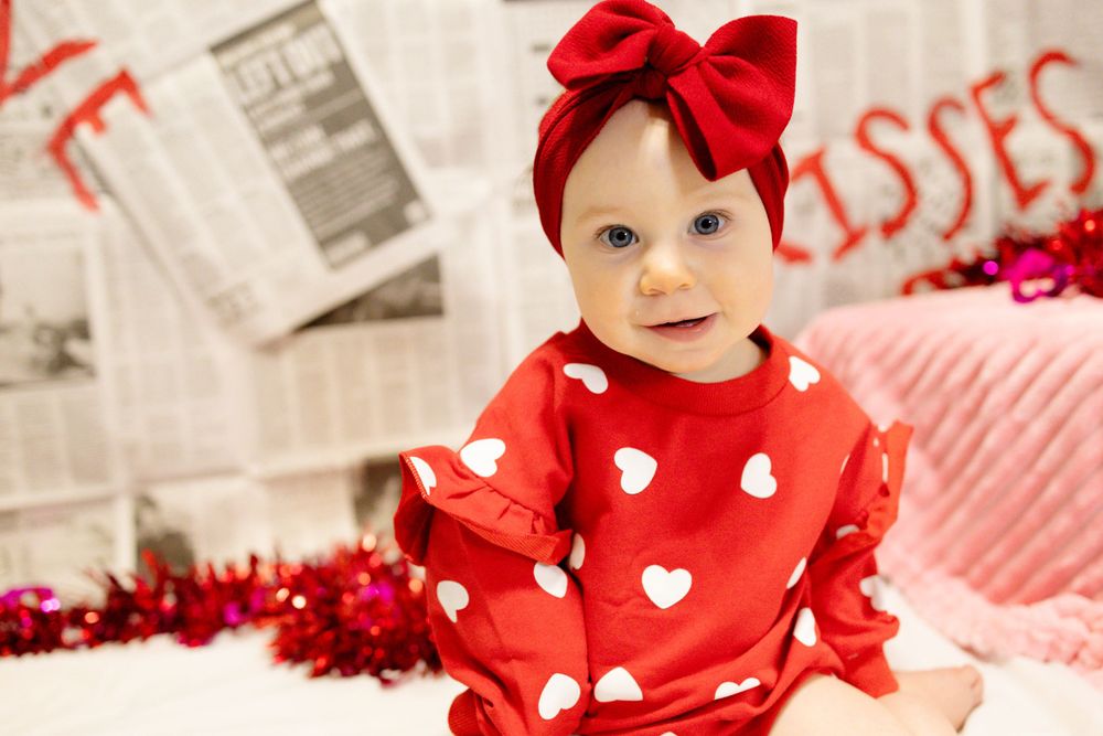 Sweet Valentine's portrait in red heart-print outfit with bow against vintage newspaper backdrop.