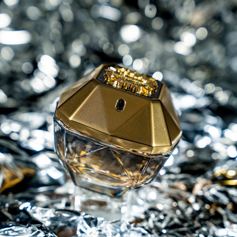 Luxury gold perfume bottle photographed with sparkling bokeh reflections in the background.