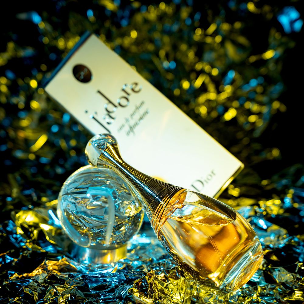 Two elegant perfume bottles surrounded by sparkling gold and blue confetti in a glamorous product shot.