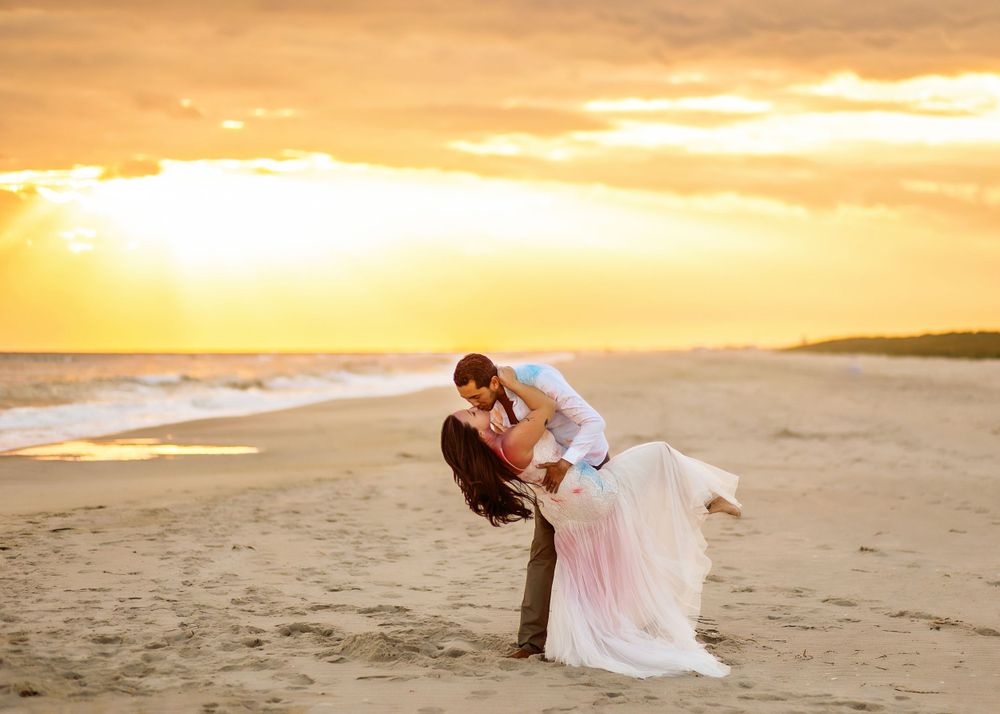 Dramatic dip pose on beach at sunset with flowing white dress.