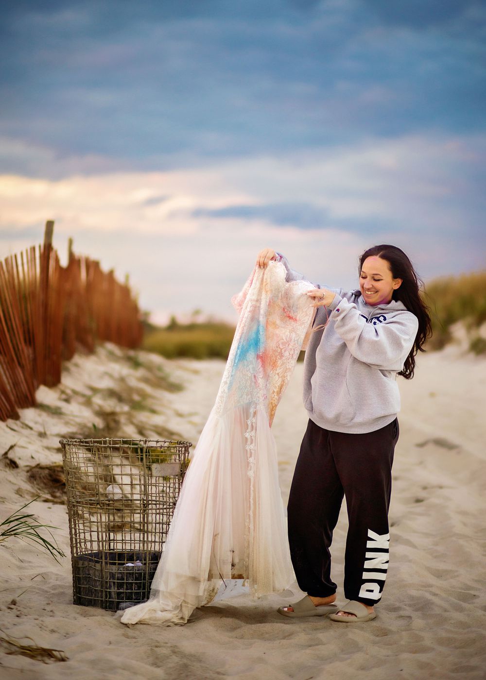 Person examining colorful stained wedding dress on beach with metal basket prop.