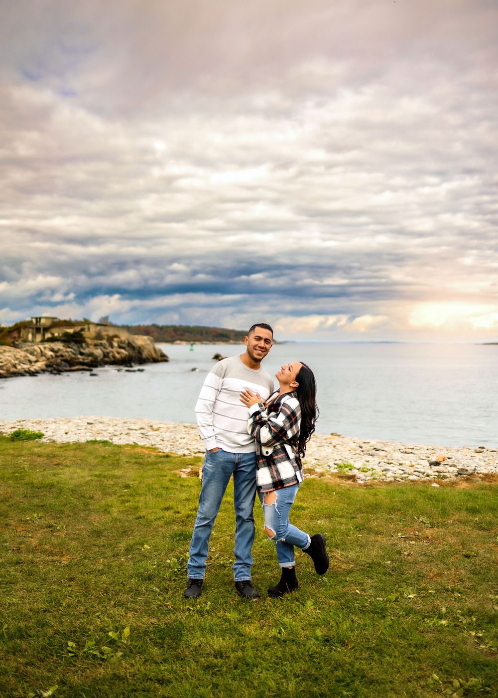 A couple shares a playful moment on grassy coastal cliffs during sunset.