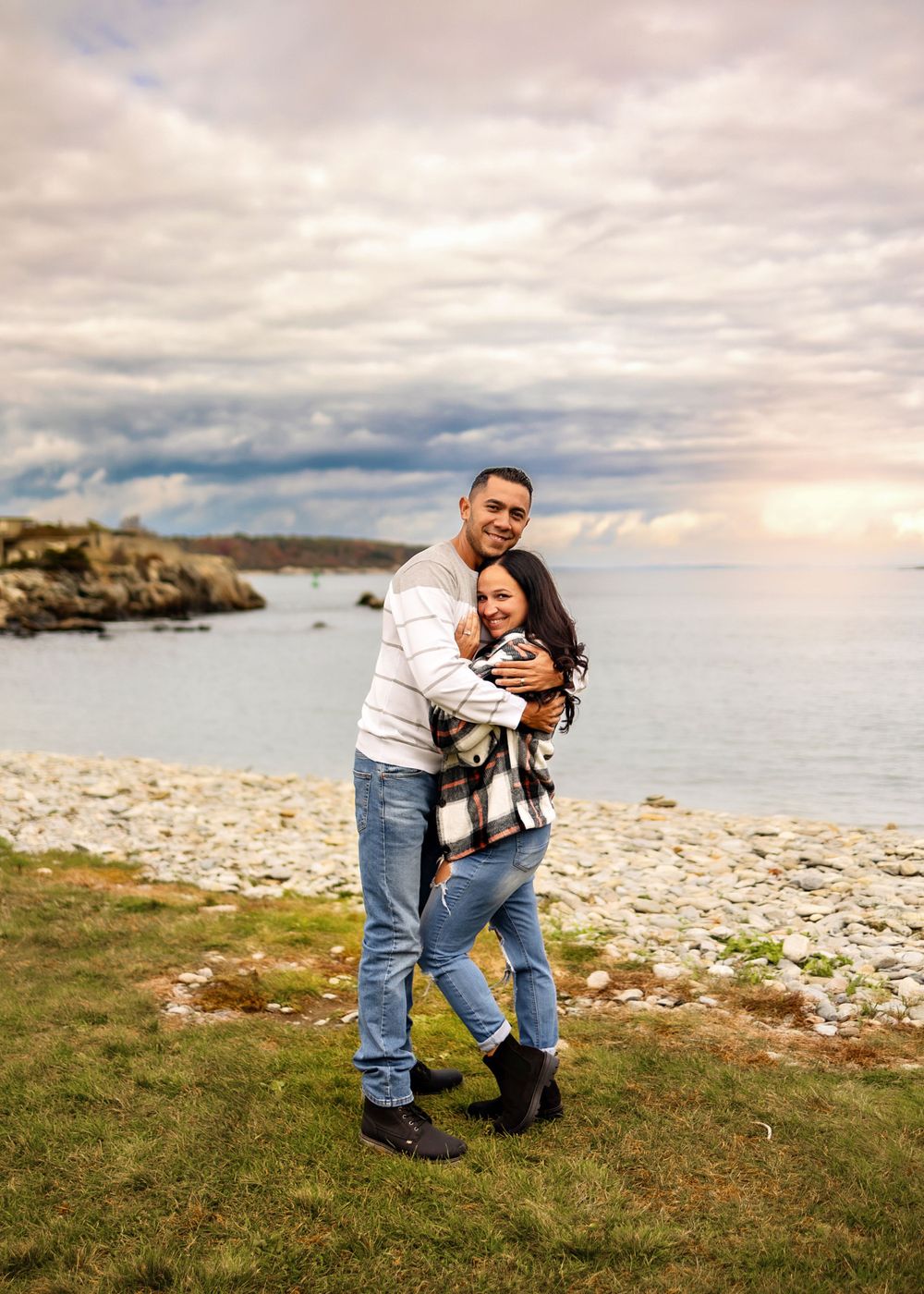 Couple embracing on a scenic coastal cliff overlooking the ocean at dusk.