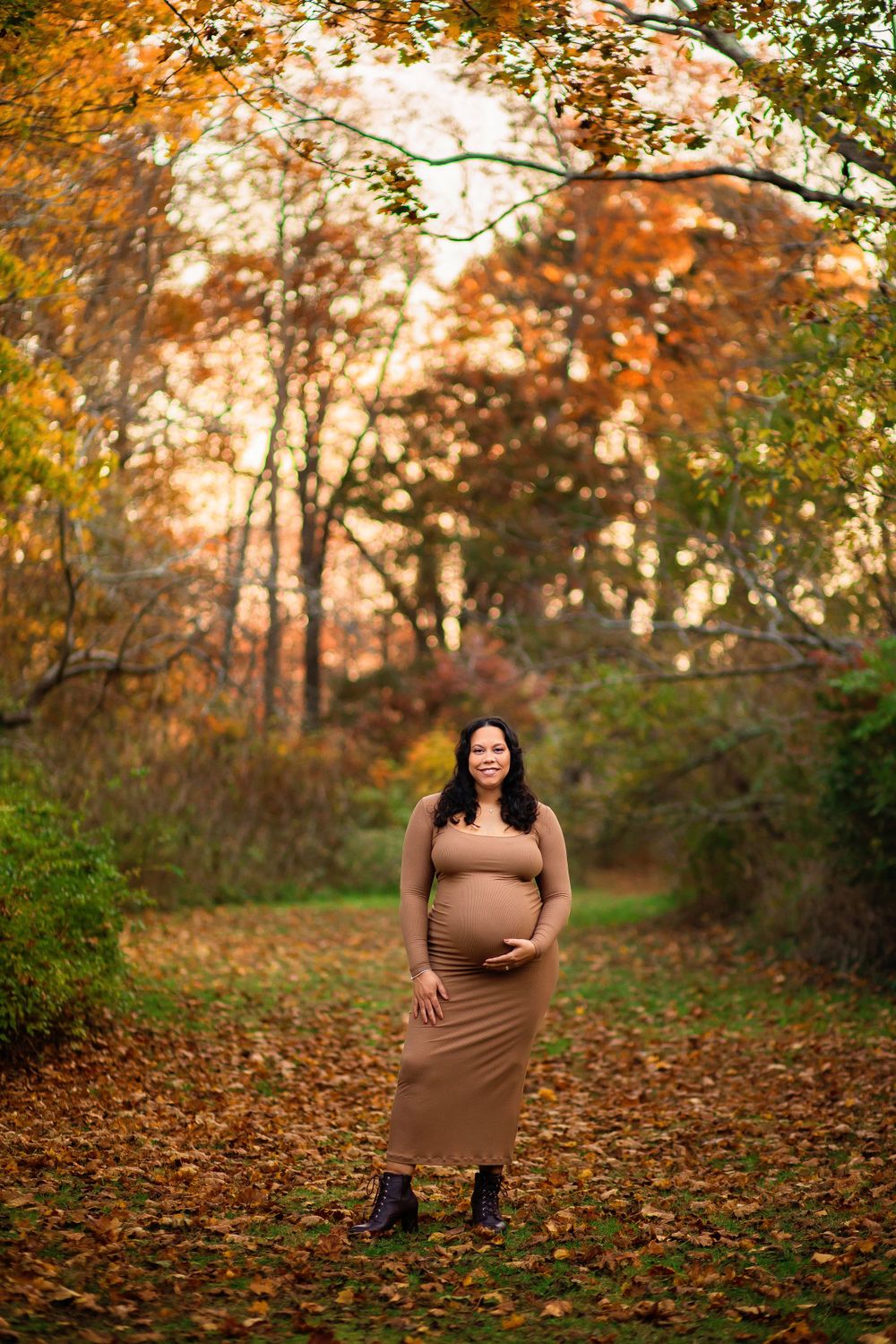 Maternity photo of woman in brown dress surrounded by fall foliage.