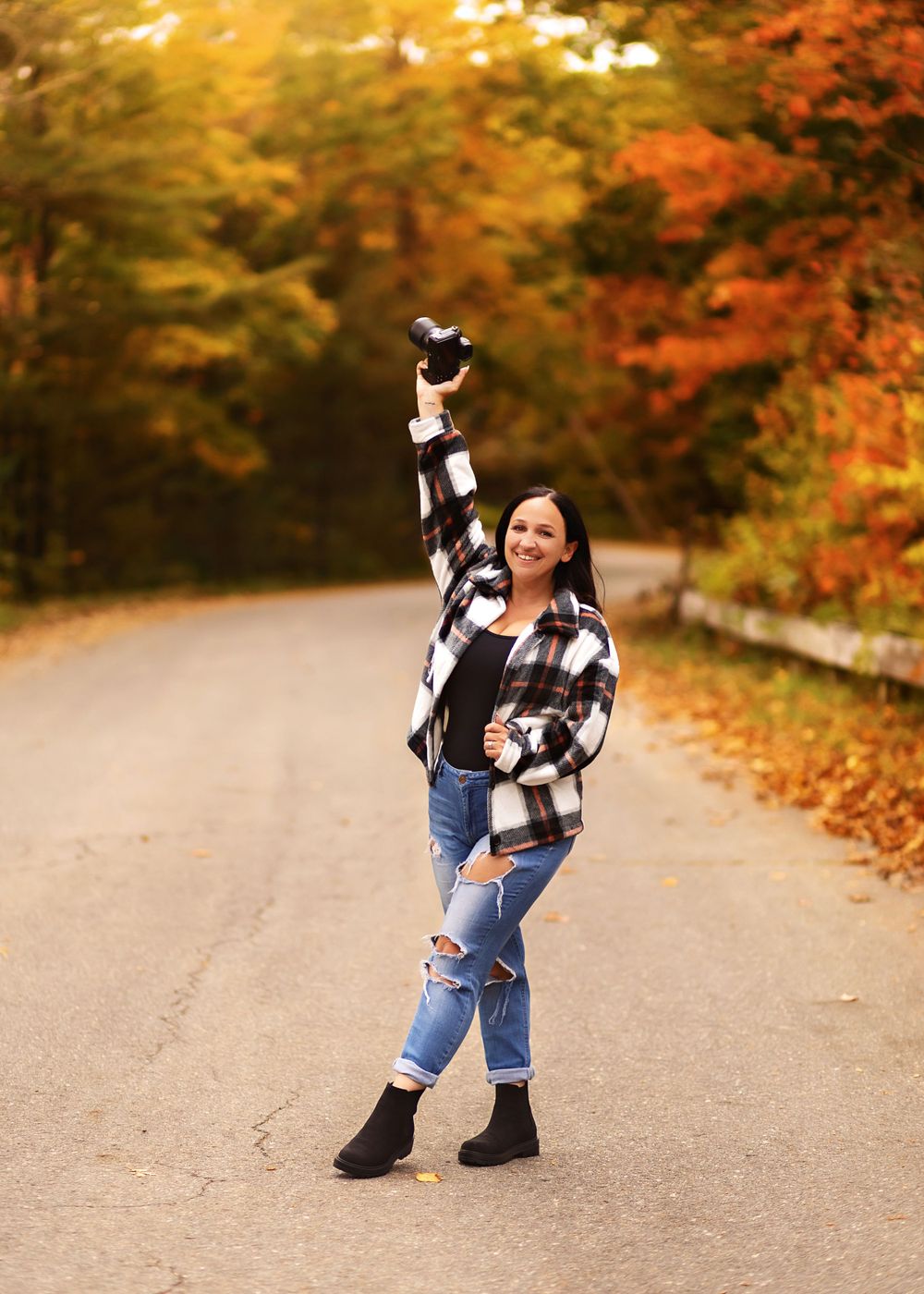 Person in plaid jacket strikes playful pose on fall road with vibrant autumn colors.